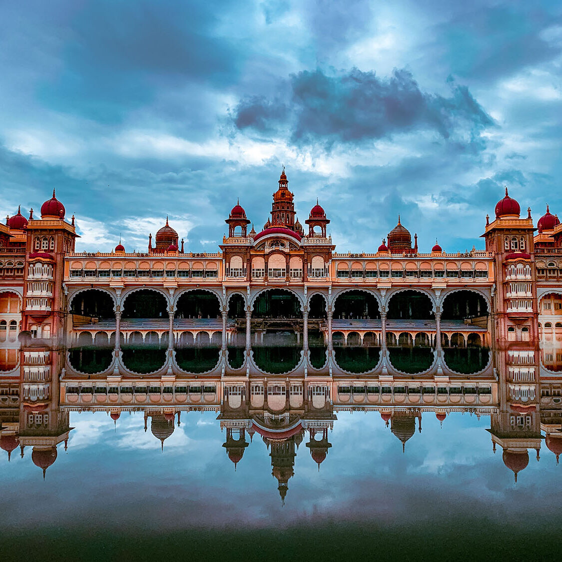 The beautiful Mysore palace of India under cloudy sky making mirror reflection in water